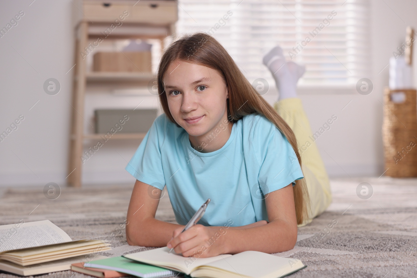 Photo of Teenage girl studying with books on floor at home