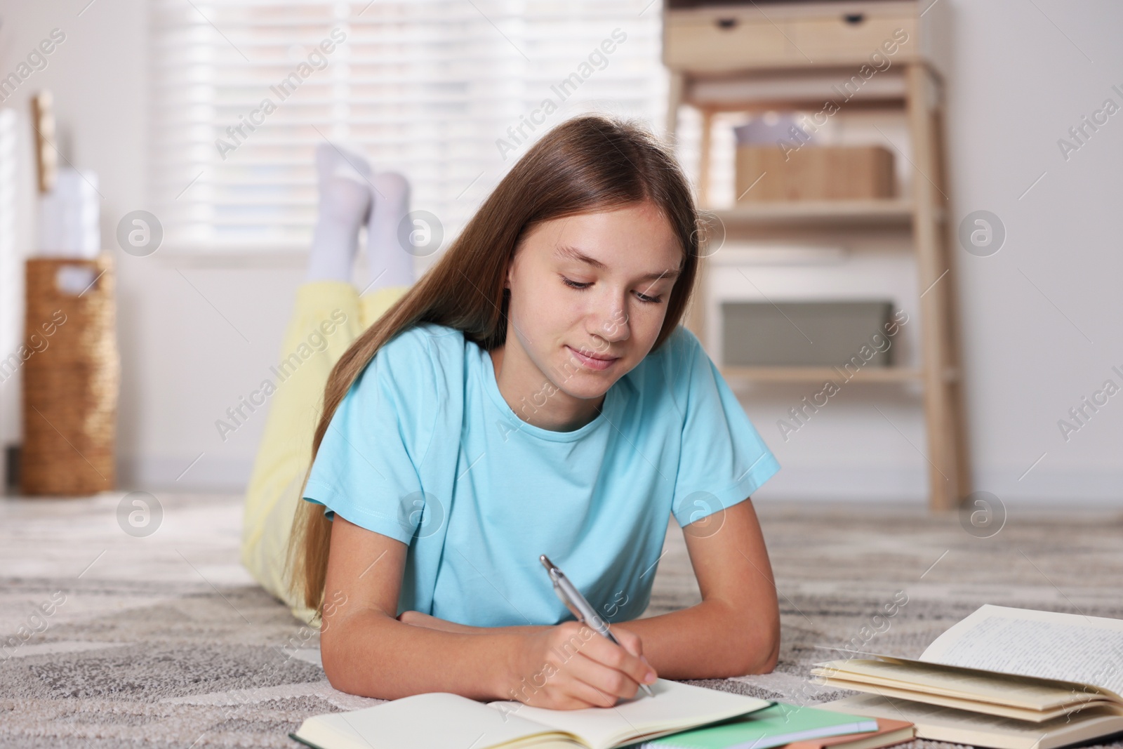 Photo of Teenage girl studying with books on floor at home