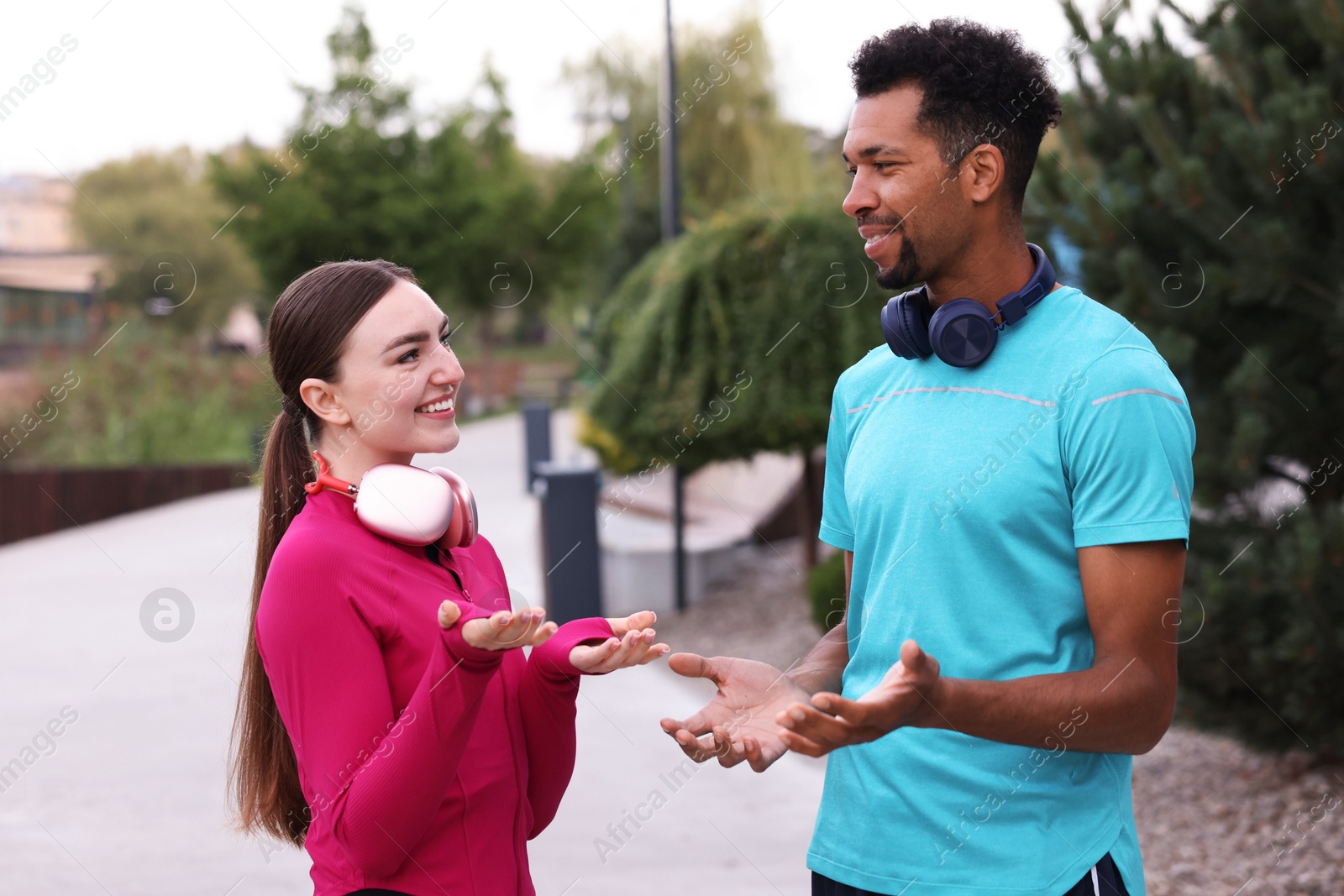 Photo of Smiling runners in sportswear with headphones talking outdoors