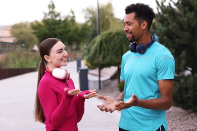 Photo of Smiling runners in sportswear with headphones talking outdoors