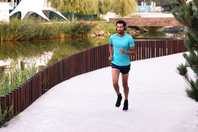 Photo of Handsome man in headphones running near river outdoors