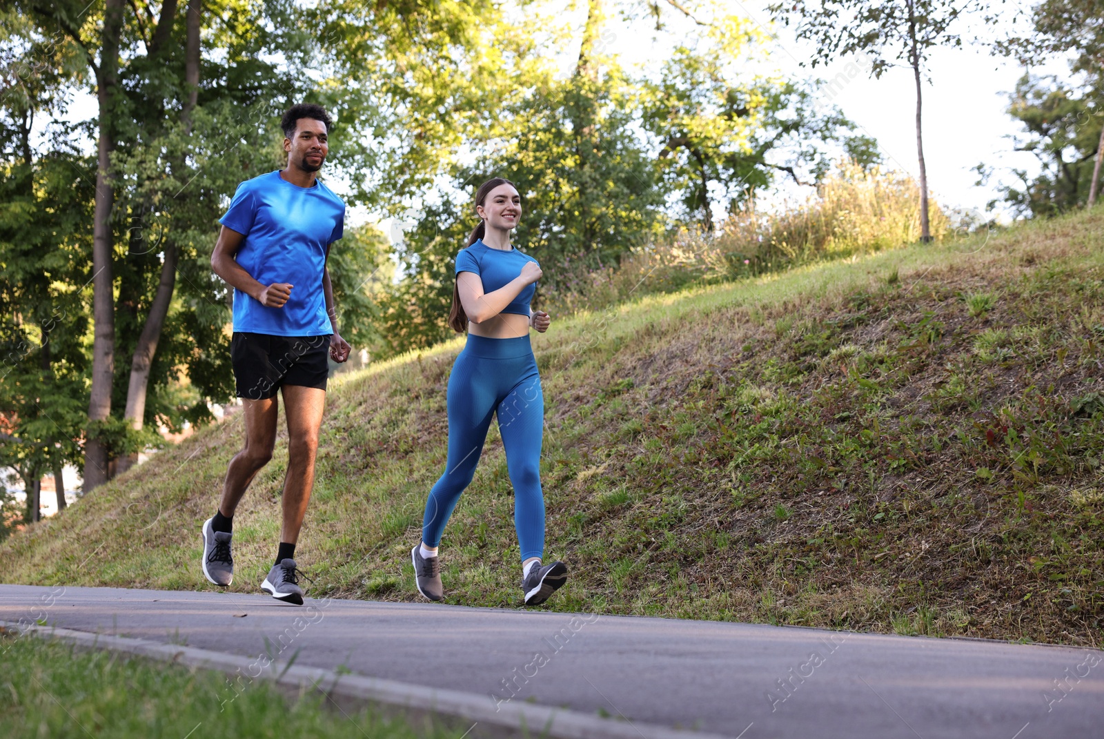 Couple in sportswear running in park, low angle view. Space for text Photo of Couple in sportswear running in park, low angle view. Space for text