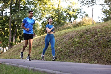 Photo of Couple in sportswear running in park, low angle view. Space for text