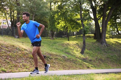 Photo of Smiling man in sportswear running in park. Space for text