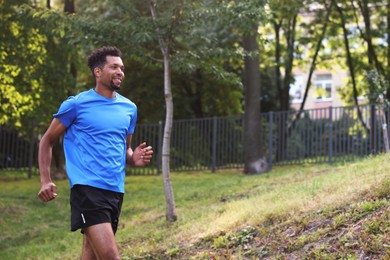 Photo of Smiling man in sportswear running in park, low angle view. Space for text
