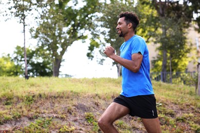Photo of Smiling man in sportswear running in park, low angle view. Space for text