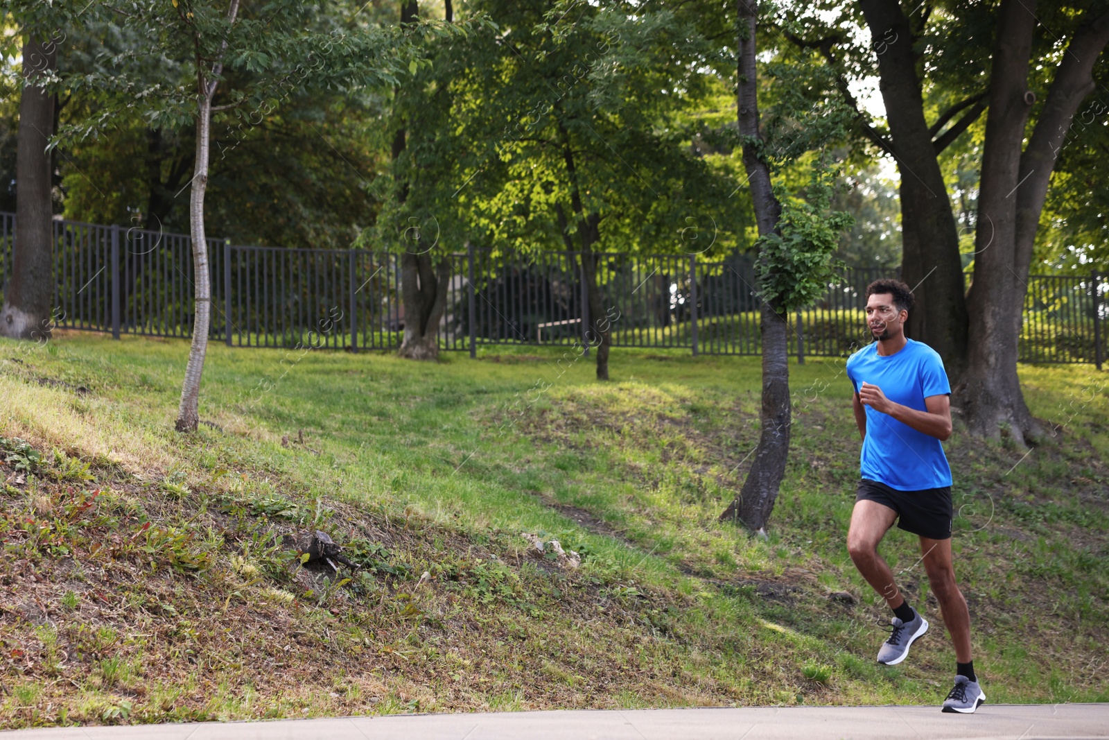 Photo of Handsome man in sportswear running in park. Space for text