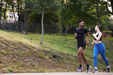 Photo of Couple in sportswear running in park, low angle view. Space for text