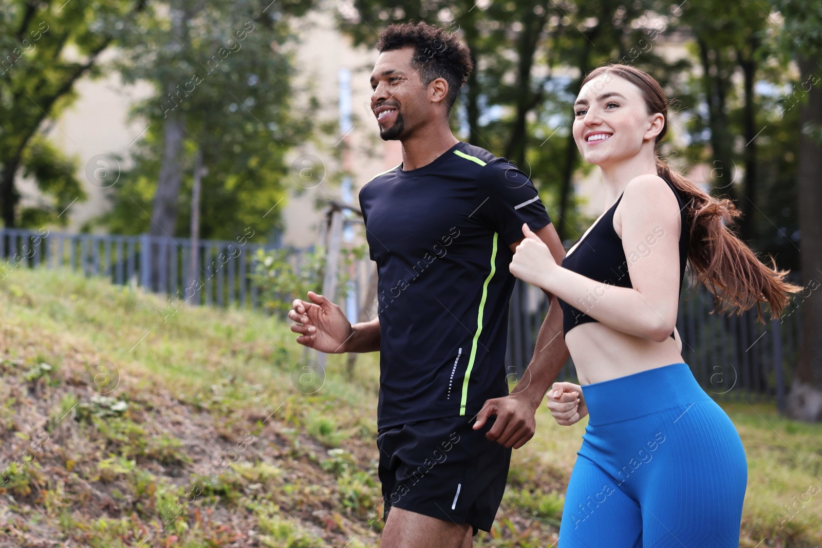 Photo of Smiling couple in sportswear running in park, low angle view. Space for text