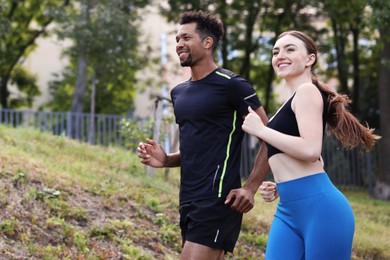 Photo of Smiling couple in sportswear running in park, low angle view. Space for text