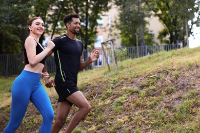 Photo of Smiling couple in sportswear running in park, low angle view. Space for text
