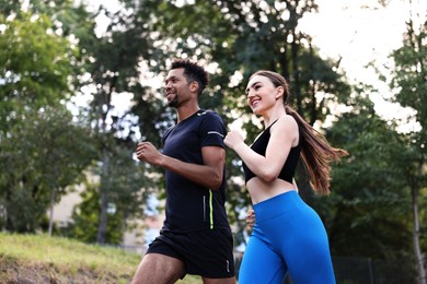 Photo of Smiling couple in sportswear running in park, low angle view