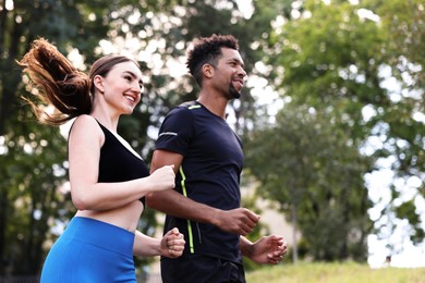 Photo of Smiling couple in sportswear running in park, low angle view. Space for text