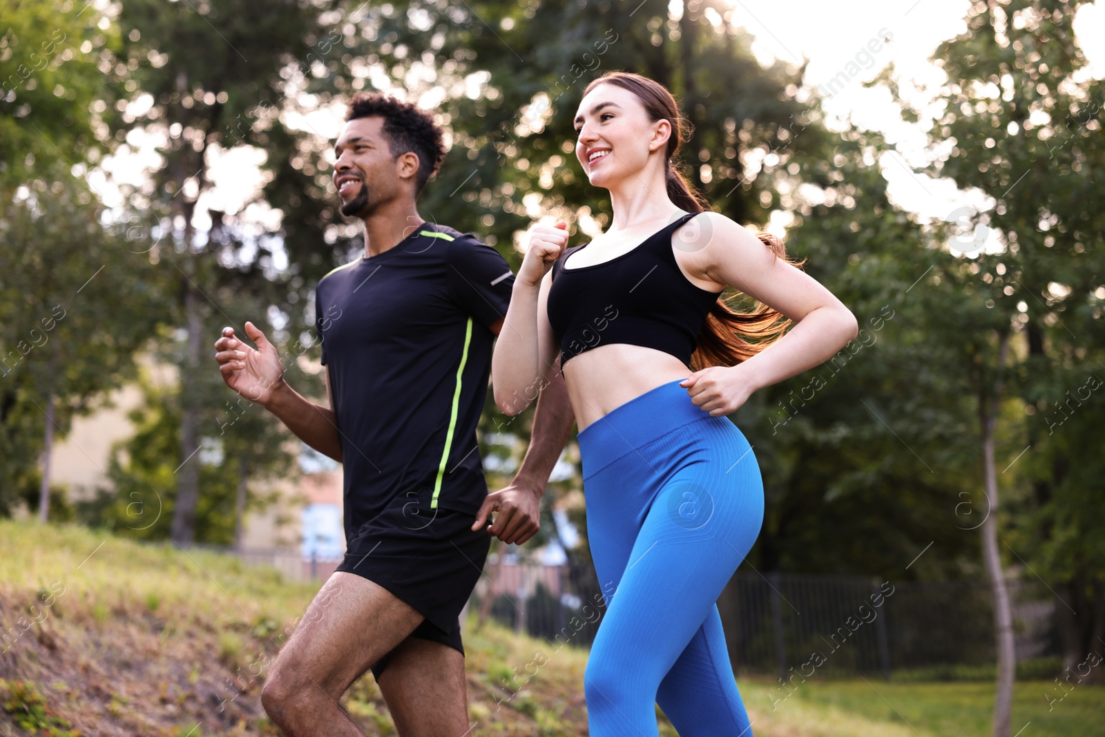 Photo of Smiling couple in sportswear running in park, low angle view