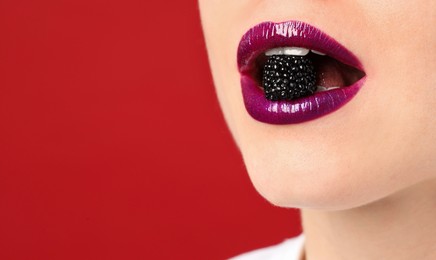 Photo of Woman with beautiful lips makeup and blackberry on red background, closeup. Space for text