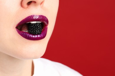 Photo of Woman with beautiful lips makeup and blackberry on red background, closeup. Space for text