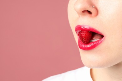 Photo of Woman with beautiful lips makeup and raspberry on dusty pink background, closeup. Space for text
