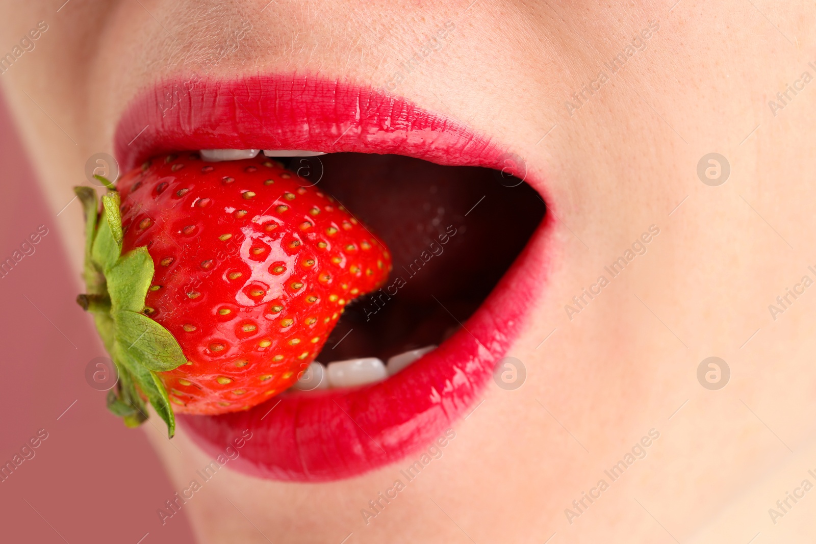 Woman with beautiful lips makeup and strawberry on dusty pink background, closeup Photo of Woman with beautiful lips makeup and strawberry on dusty pink background, closeup
