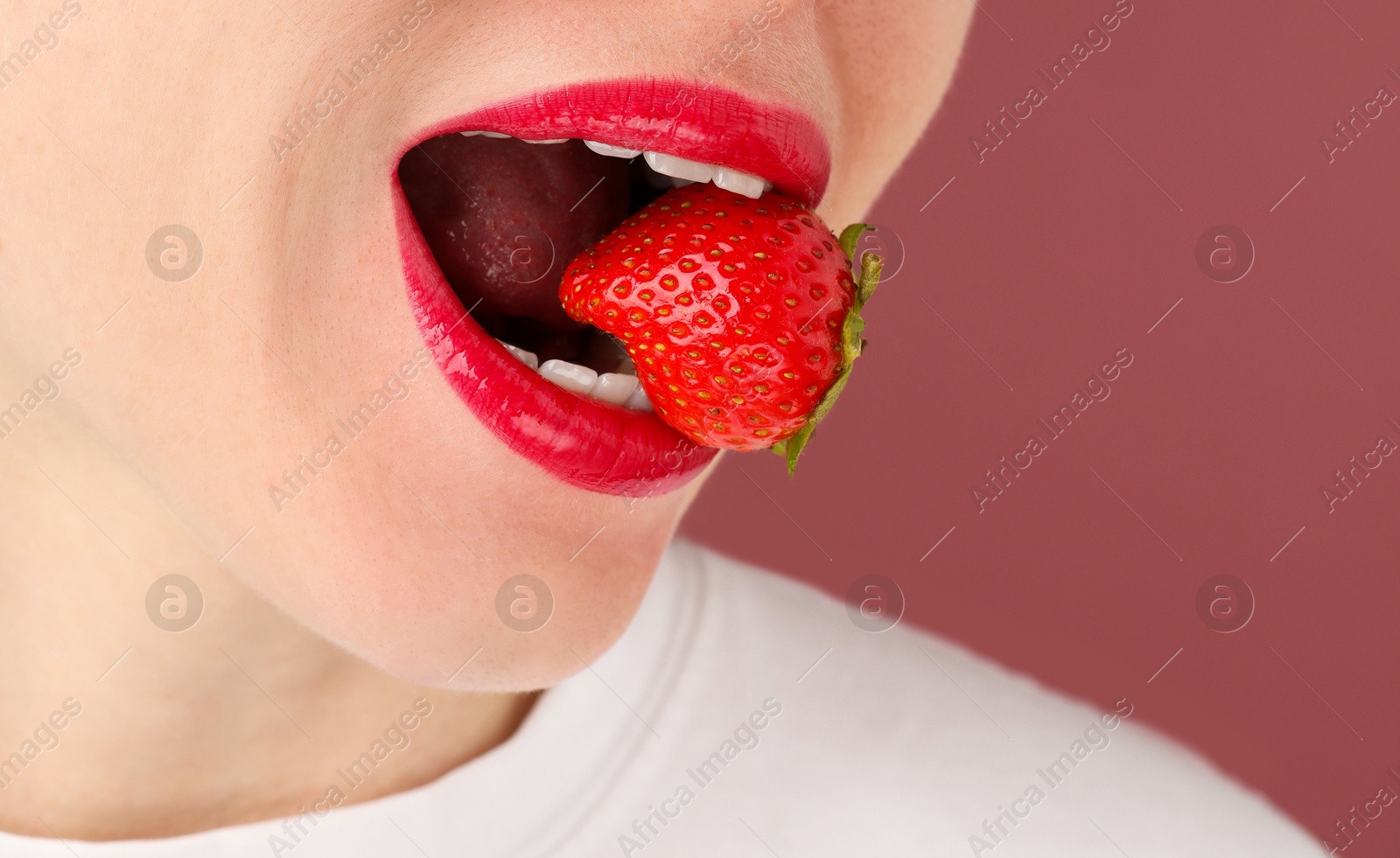 Woman with beautiful lips makeup and strawberry on dusty pink background, closeup. Space for text Photo of Woman with beautiful lips makeup and strawberry on dusty pink background, closeup. Space for text
