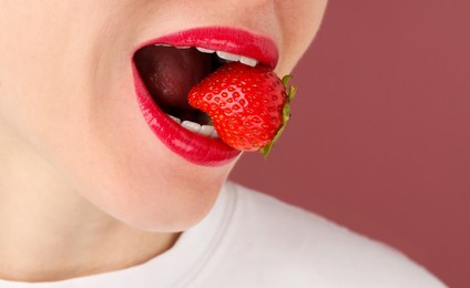 Photo of Woman with beautiful lips makeup and strawberry on dusty pink background, closeup. Space for text