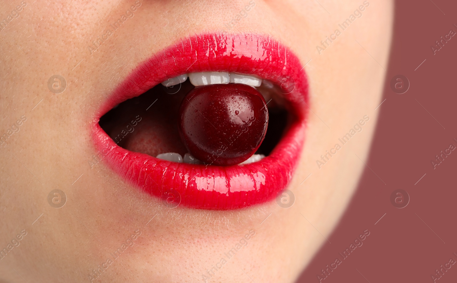Woman with beautiful lips makeup and cherry on dusty pink background, closeup Photo of Woman with beautiful lips makeup and cherry on dusty pink background, closeup