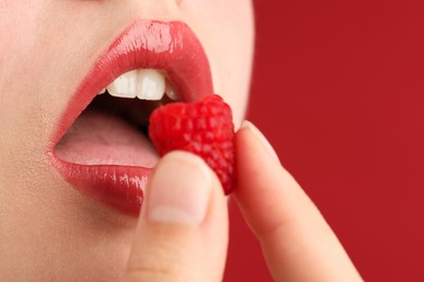 Photo of Woman with beautiful lips makeup and raspberry on red background, closeup. Space for text