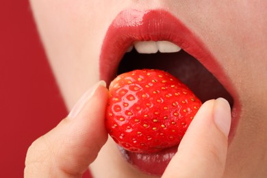 Photo of Woman with beautiful lips makeup and strawberry on red background, closeup