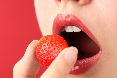 Photo of Woman with beautiful lips makeup and strawberry on red background, closeup