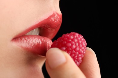 Photo of Woman with beautiful lips makeup and raspberry candy on black background, closeup