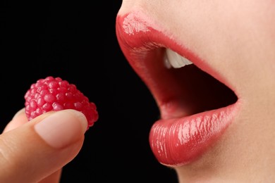 Photo of Woman with beautiful lips makeup and raspberry candy on black background, closeup