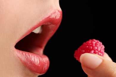 Photo of Woman with beautiful lips makeup and raspberry candy on black background, closeup