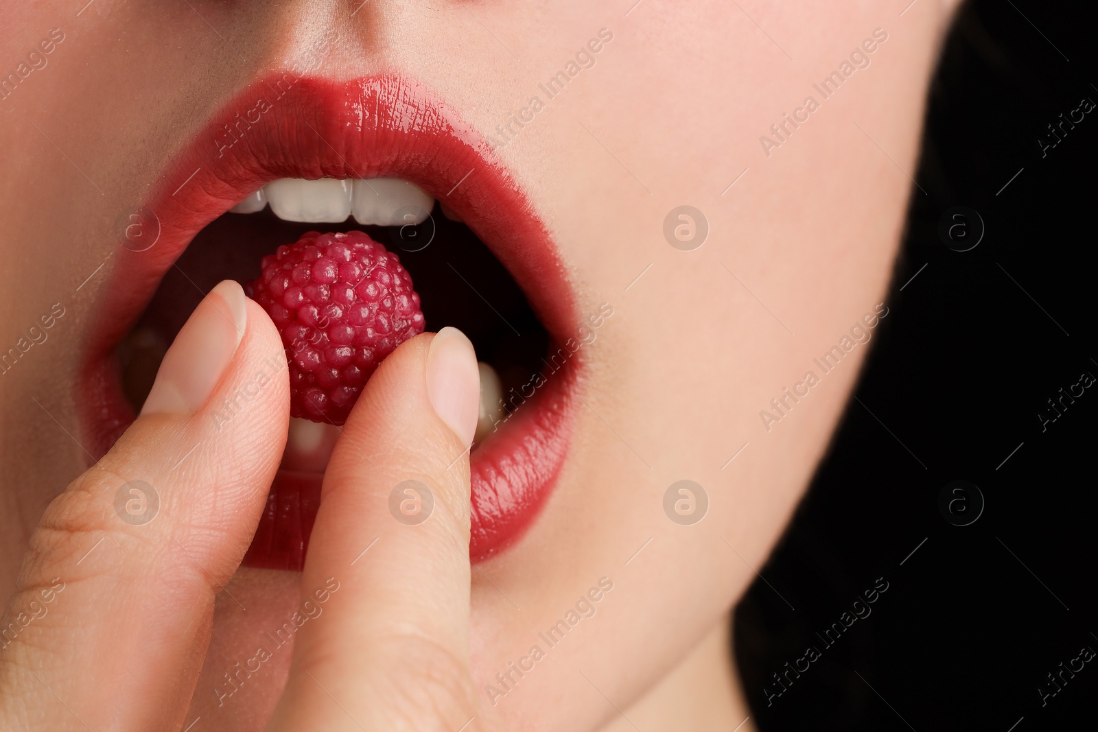 Photo of Woman with beautiful lips makeup and raspberry candy on black background, closeup