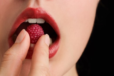 Photo of Woman with beautiful lips makeup and raspberry candy on black background, closeup