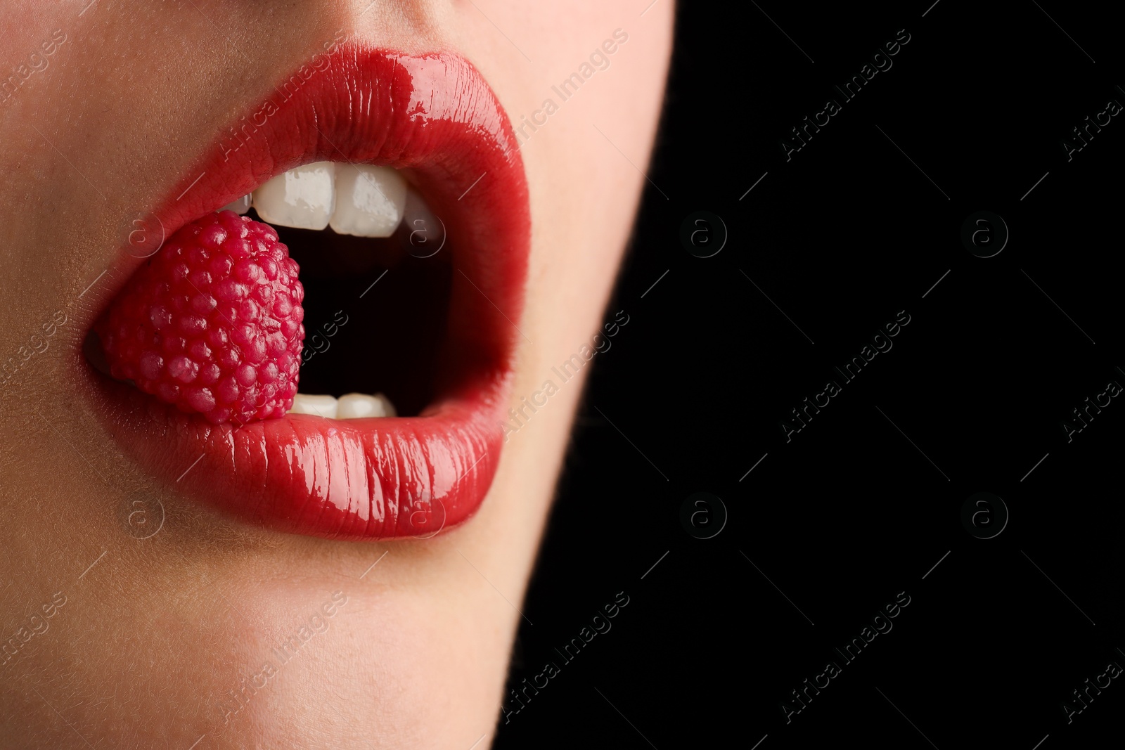 Photo of Woman with beautiful lips makeup and raspberry candy on black background, closeup. Space for text