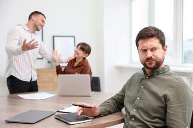 Photo of Man feeling jealous of his colleague's success in office, selective focus