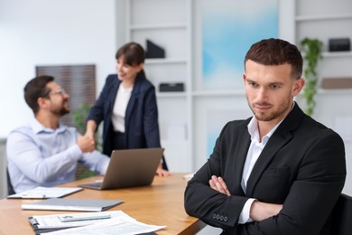 Photo of Man feeling jealous of his successful colleague receiving congratulations in office, selective focus