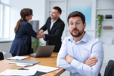Photo of Man feeling jealous of his successful colleague receiving congratulations in office, selective focus