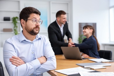 Photo of Man feeling jealous of his successful colleague receiving congratulations in office, selective focus