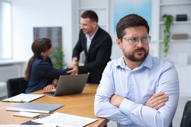 Photo of Man feeling jealous of his successful colleague receiving congratulations in office, selective focus