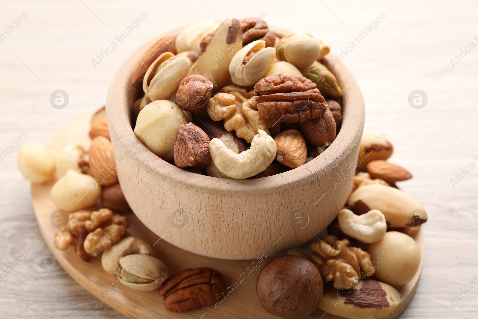 Photo of Mix of different nuts in bowl on wooden table, closeup