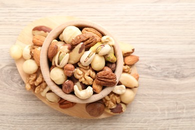 Photo of Mix of different nuts in bowl on wooden table, top view