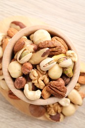 Photo of Mix of different nuts in bowl on wooden table, top view