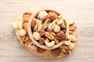 Photo of Mix of different nuts in bowl on wooden table, top view