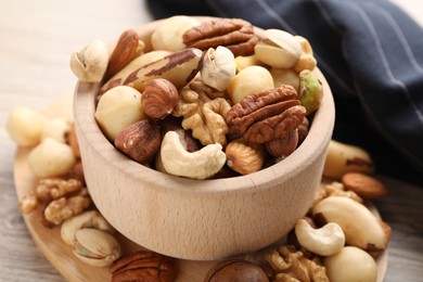 Photo of Mix of different nuts in bowl on wooden table, closeup