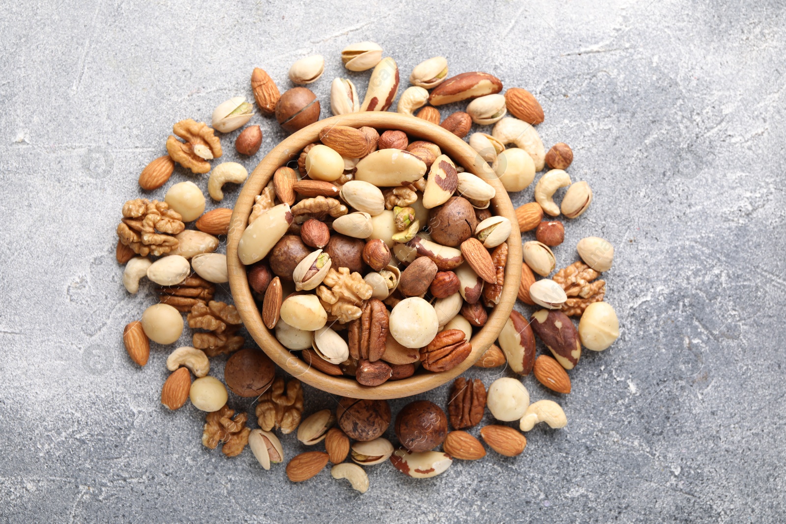 Photo of Mix of different nuts in bowl on grey textured table, top view