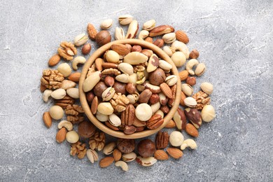 Photo of Mix of different nuts in bowl on grey textured table, top view