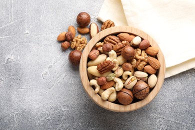Photo of Mix of different nuts in bowl on grey textured table, top view. Space for text