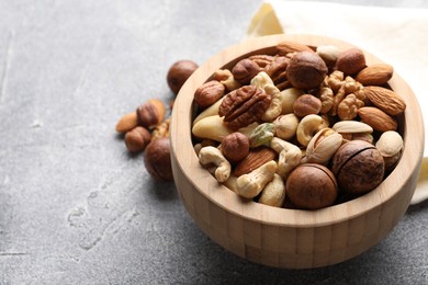 Photo of Mix of different nuts in bowl on grey textured table, closeup. Space for text