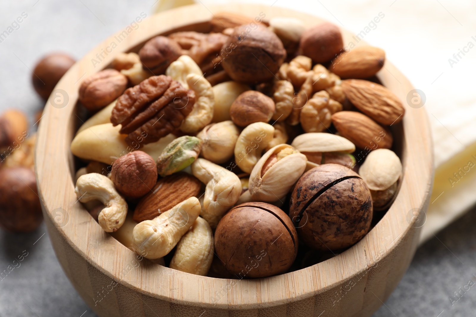 Photo of Mix of different nuts in bowl on grey table, closeup