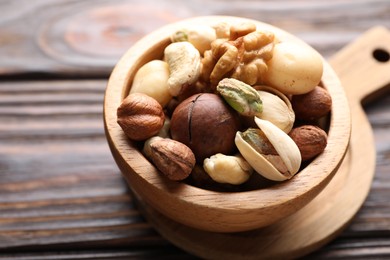 Photo of Mix of different nuts in bowl on wooden table, closeup